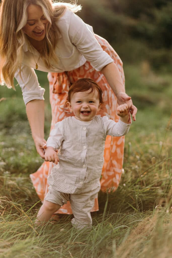 Little boy is standing and mum is holding him. He is smiling to his dad. Lovely candid photograph during family photo shoot in Hampshire. Ewa Jones Photography