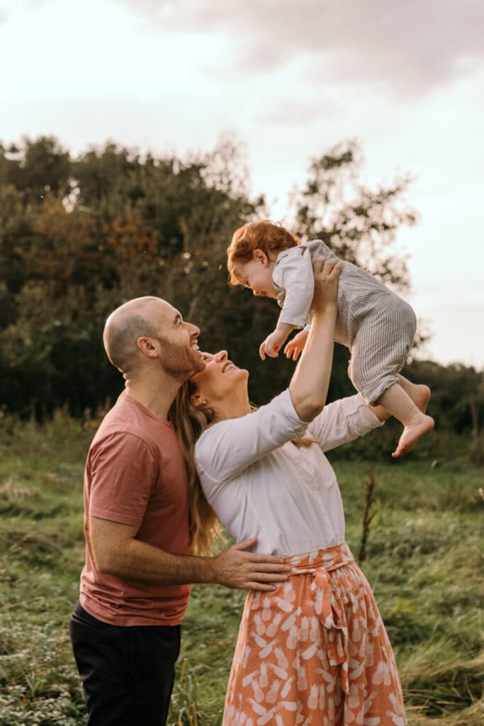 family photo session in the fields in Hampshire. Mum is lifting up her son in the air and dad is standing behind. they are all laughing. Family photographer in Hampshire. Ewa Jones Photography