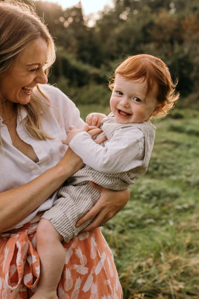 Mum is tickling her boy on his tummy and laughing. Boy is laughing too. Lovely summer sunset family photo session in Hampshire. Ewa Jones Photography