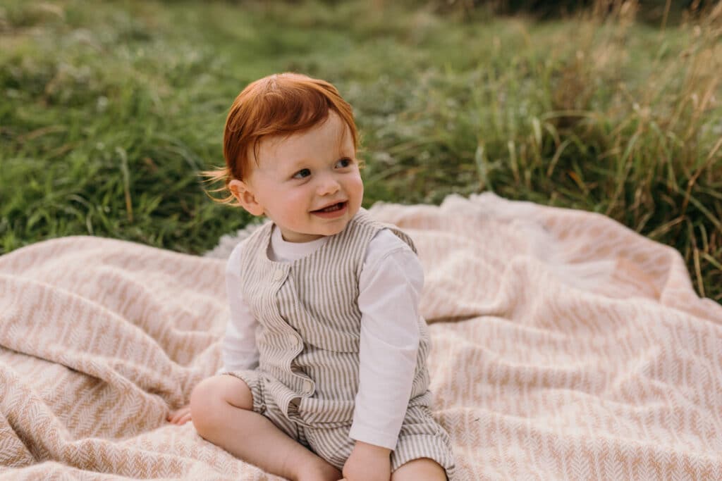 boy is sitting on the blanket and looking away. he is wearing lovely stripy outfit. Natural family photo shoot in Hampshire. Ewa Jones Photography