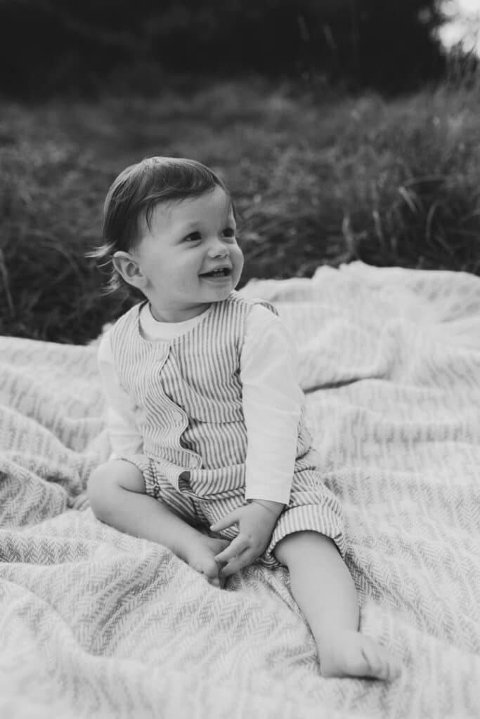 boy is sitting on the blanket and looking away. he is wearing lovely stripy outfit. Natural family photo shoot in Hampshire. Ewa Jones Photography