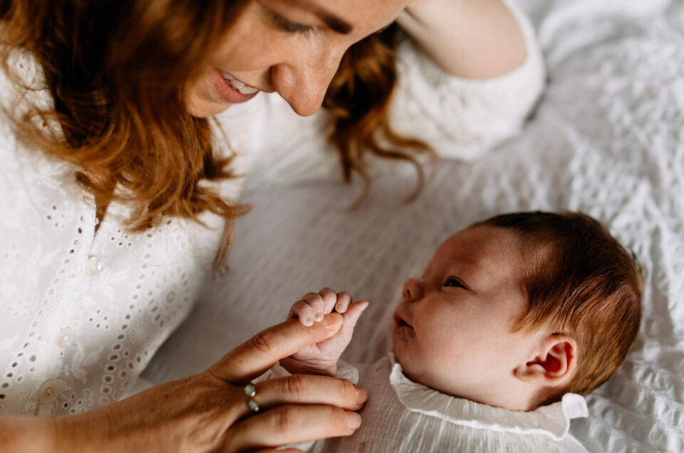 Mum and newborn baby are laying on bed. Newborn baby girl is holding her mum's finger. Newborn photo shoot in Hampshire. Beautiful newborn photo shoot at home.Ewa Jones Photography