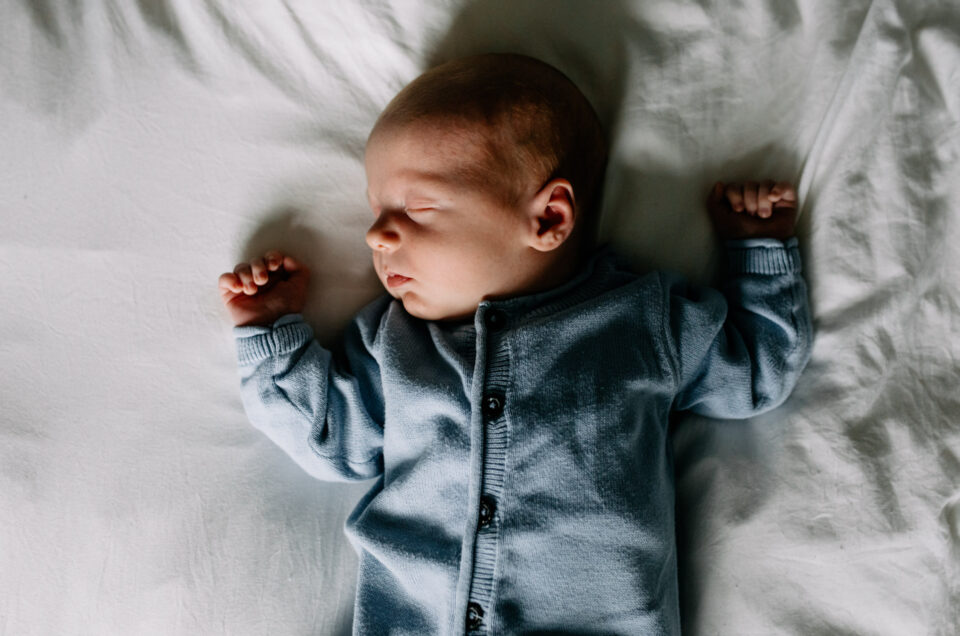 Newborn baby is sleeping on bed and has his hands up. lovely newborn photo shoot in Basingstoke, Hampshire. Newborn photoshoot. Ewa Jones Photography