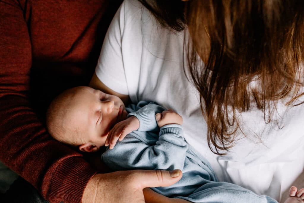 Mum and dad are sitting on the bed and cuddling their newborn baby boy. Newborn photographer in Hampshire. Ewa Jones Photography