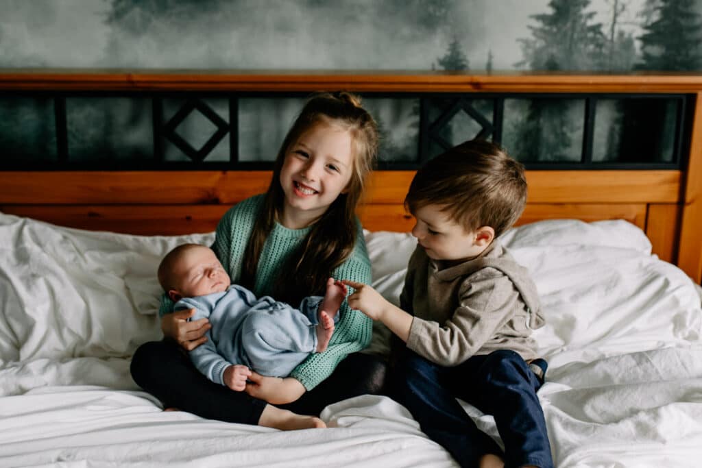 Siblings are holding newborn baby brother and smiling. Newborn photography in Hampshire. Ewa Jones Photography