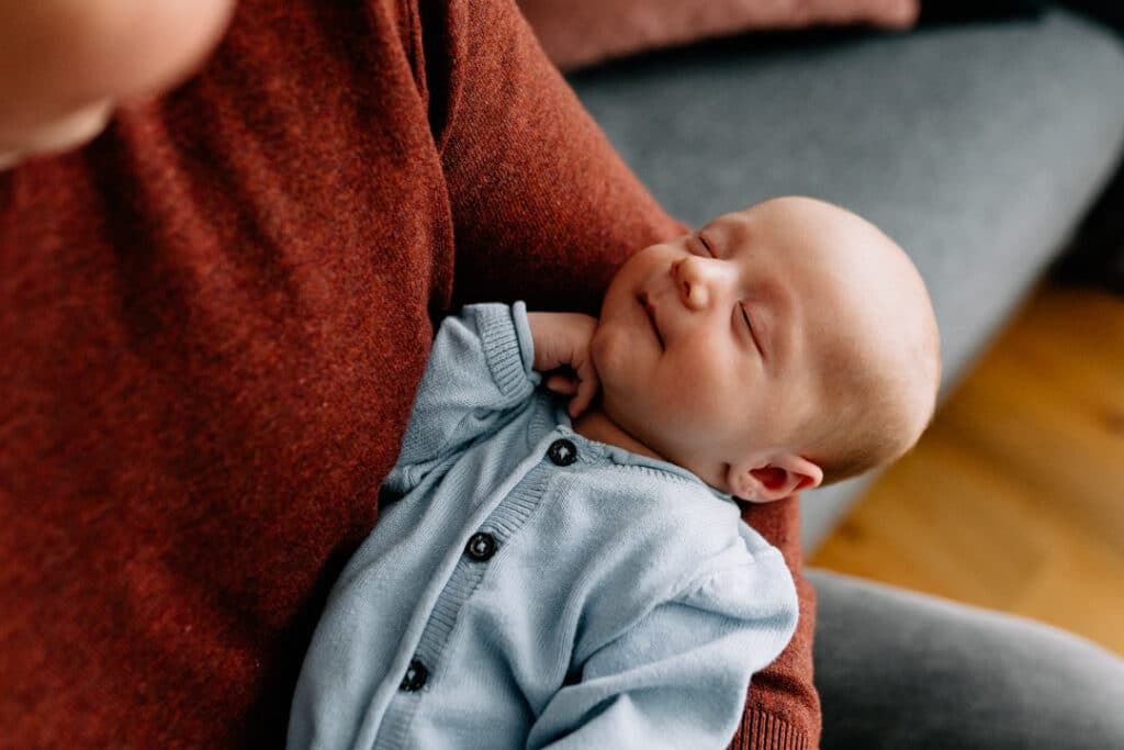 Dad is holding newborn baby boy and the boy is sleeping. he has his hand on his chin. Newborn photo shoot in Basingstoke. Ewa Jones Photography