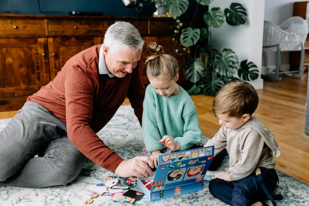 Dad is sitting on the floor and playing games with his children. Natural lifestyle family photographer in Basingstoke, Hampshire. Ewa Jones Photography