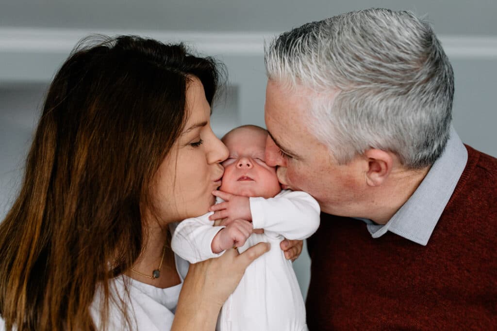 Mum and dad are kissing newborn boy boy on his cheeks. Newborn photography in Hampshire. Ewa Jones Photography