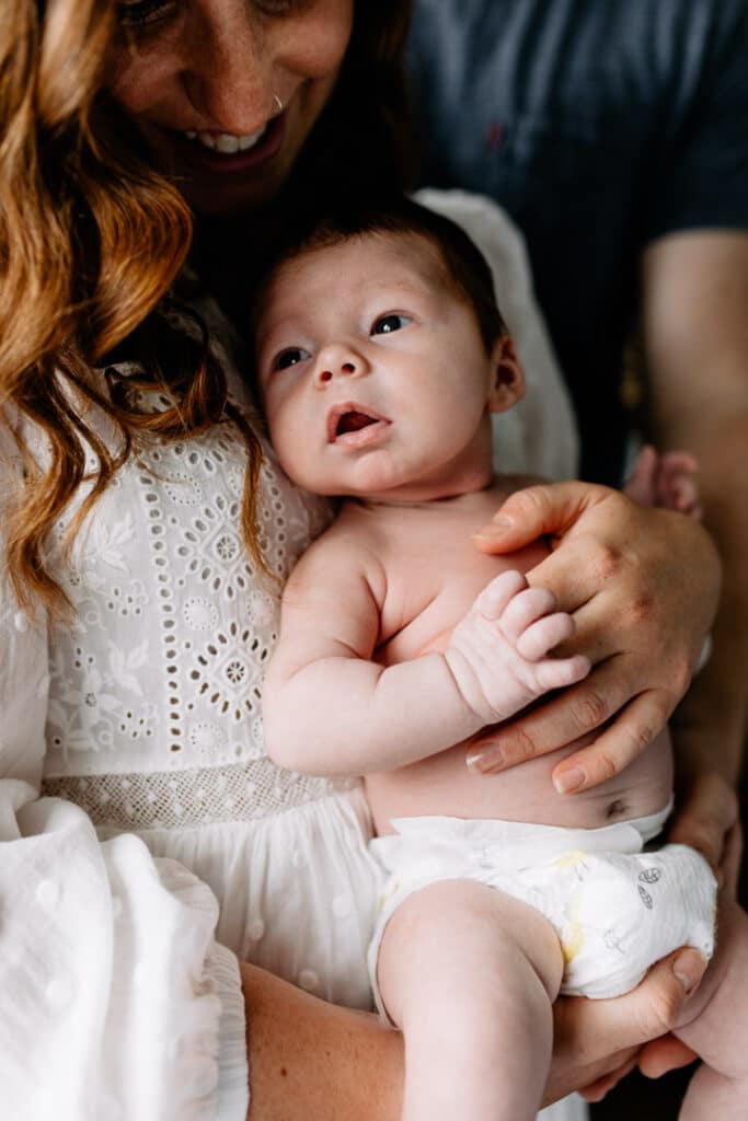 Mum is holding her newborn baby and the baby is looking in the distance. Lovely newborn photo session in Hampshire. Ewa Jones Photography