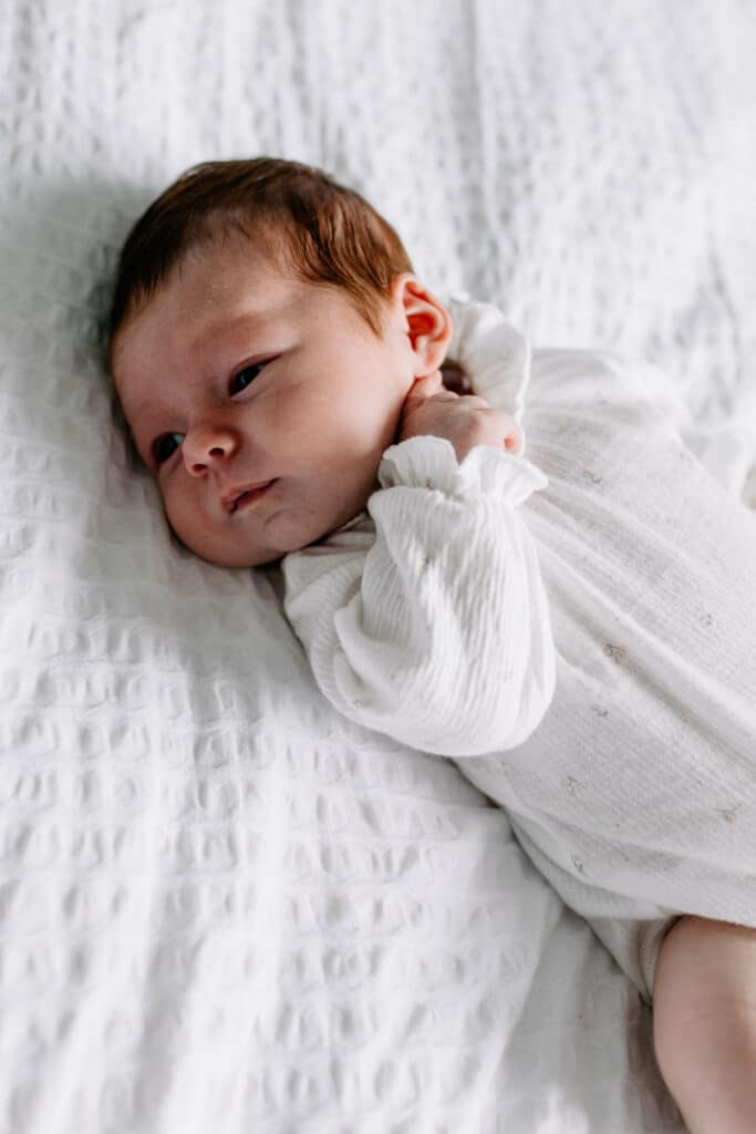 newborn baby girl is laying on bed and looking away. lovely natural lifestyle photographer in Basingstoke, Hampshire. Ewa Jones Photography