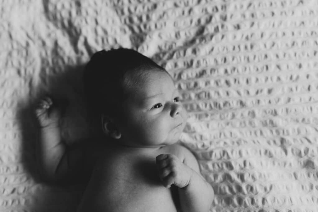 Black and white image of newborn baby girl laying on bed and looking away towards the light. Newborn photographer in Hampshire. Ewa Jones Photography
