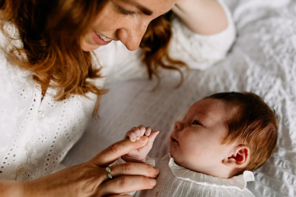 Mum and newborn baby are laying on bed. Newborn baby girl is holding her mum's finger. Newborn photo shoot in Hampshire. Ewa Jones Photography