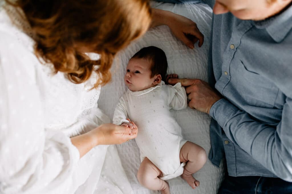 Mum, dad and newborn baby are laying on bed. Newborn baby girl is looking up at her mum. Newborn photographer in Hampshire. Ewa Jones Photography