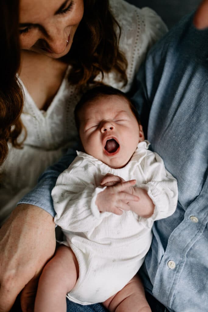 Newborn baby girl is yawning. She is wearing lovely white baby grow. Natural lifestyle newborn photography in Hampshire. Ewa Jones Photography