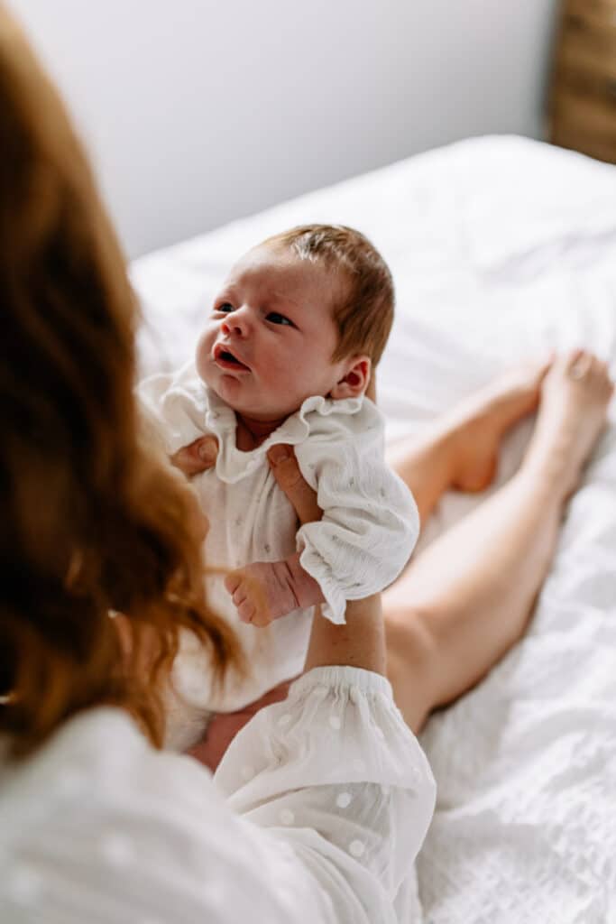 Mum is holding her newborn baby girl and the baby is looking up at her mum. Newborn photo shoot in Hampshire. Ewa Jones Photography