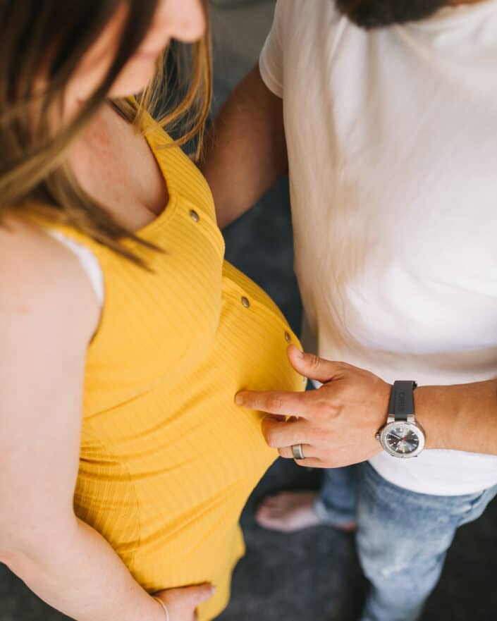 pregnant mum is standing and dad is close to her. He is touching baby bump with his fingers. Intimate maternity photo shoot in Basingstoke, Hampshire. Ewa Jones Photography