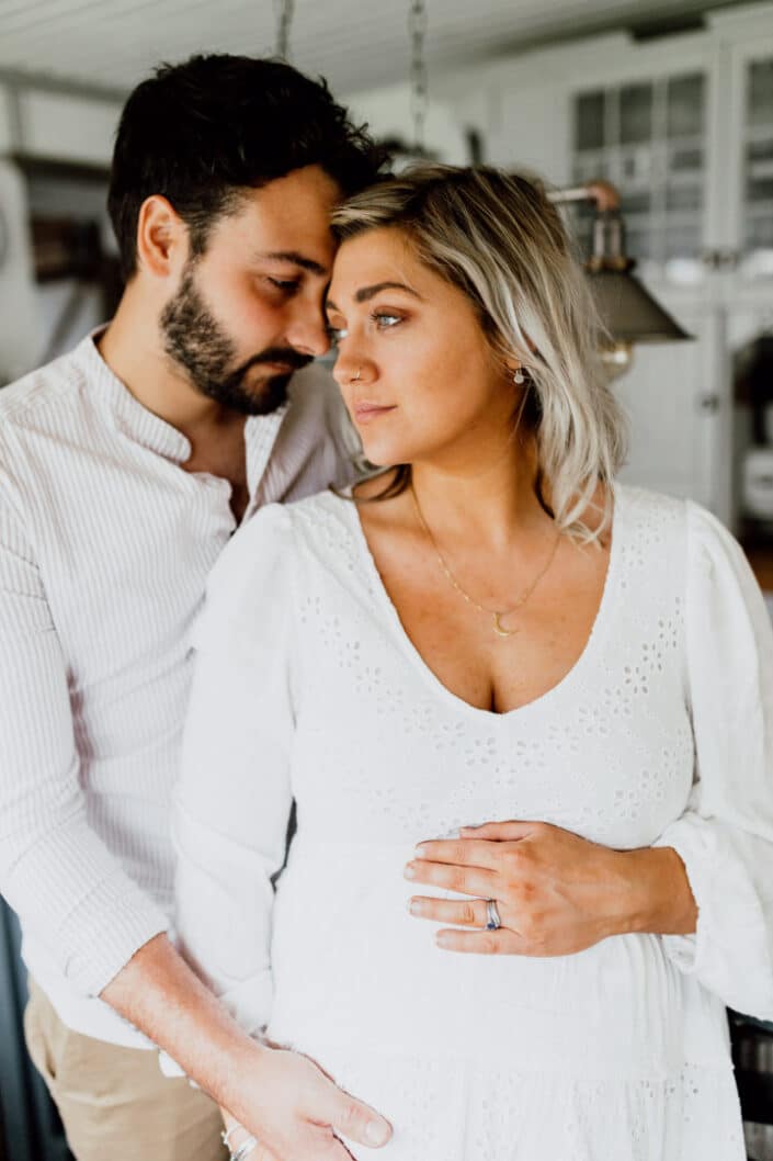 Expecting parents are standing next to each other and mum is looking away. dad is standing behind and holdling baby bump. Maternity photo shoot in Hampshire. Ewa Jones Photography