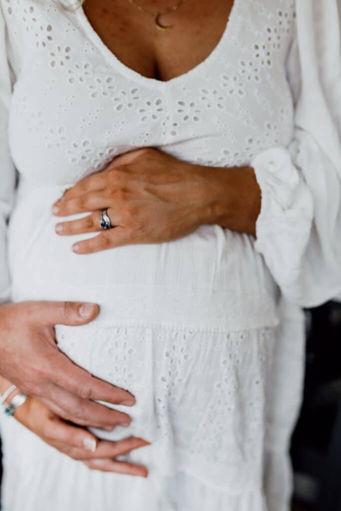 Expecting mum is wearing lovely white boho dress and holding her baby bump. Maternity photographer in Hampshire. Basingstoke photographer. Ewa Jones Photography