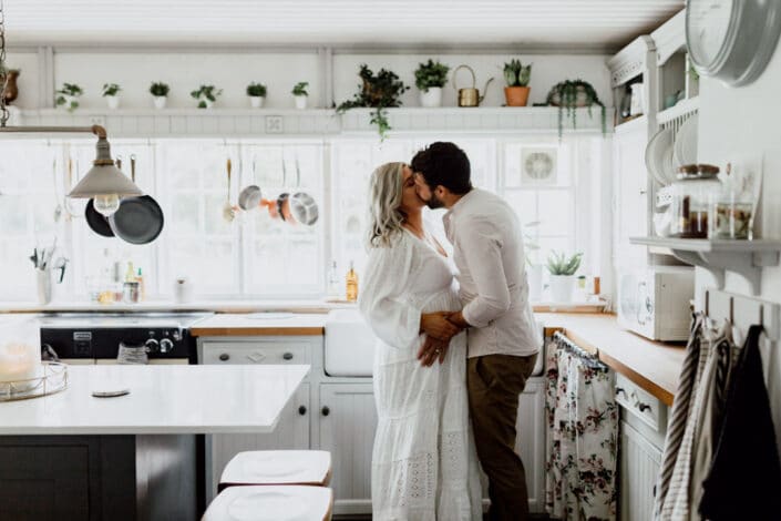 Expecting parents are standing in the kitchen and kissing. They have a lovely farm house. Maternity photographer in Hampshire. Ewa Jones Photography
