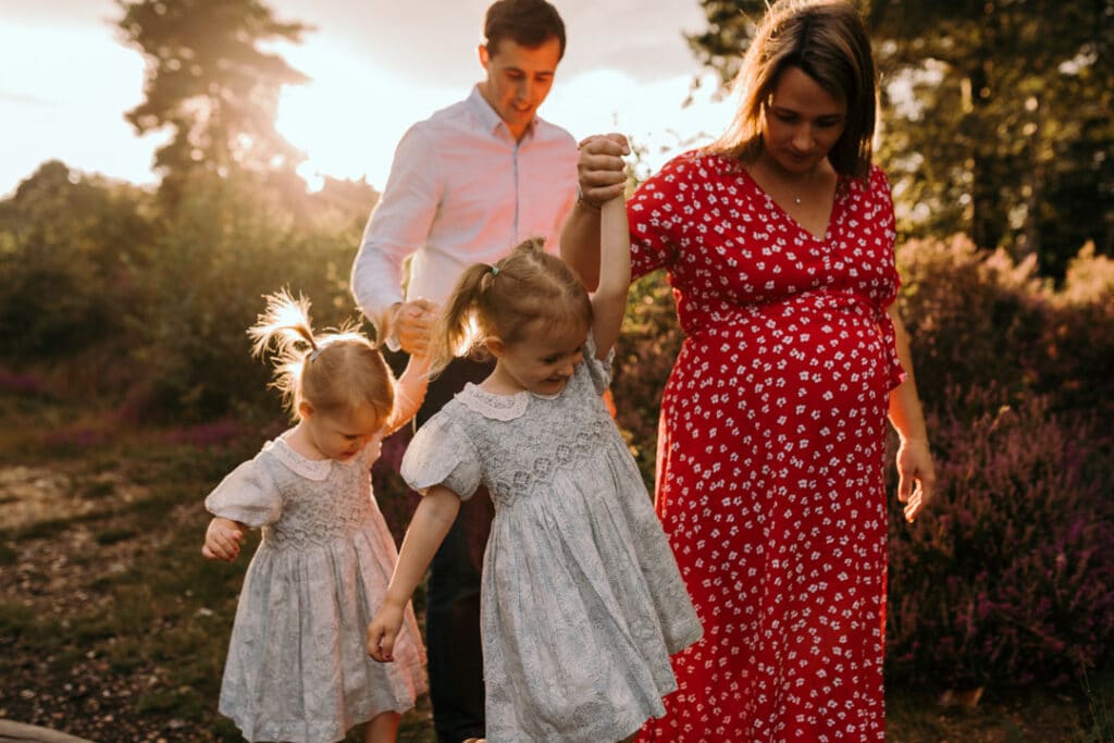 Expecting parents are walking and holding hands with their two older daughters. Natural lifestyle maternity photo shoot in Hampshire. Ewa Jones Photography