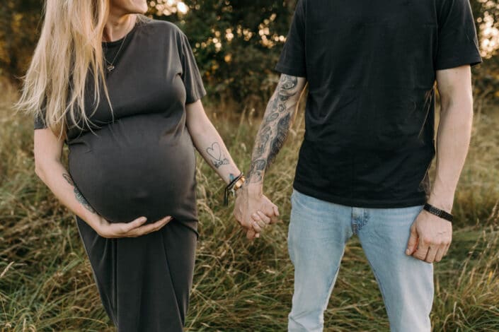 Pregnant mum is holding hands with her husband and mum is holding her bump. Maternity photo shoot in the fields. Ewa Jones Photography