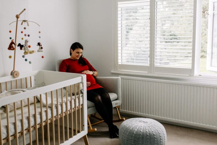 Pregnagnt mum is sitting on the chair in the baby nursery. She is looking down at the baby bump. Maternity photo shoot in London. Ewa Jones Photography