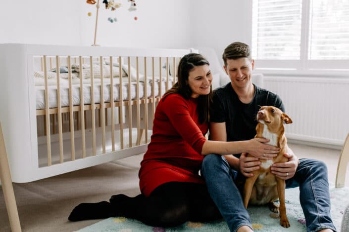 Expecting parents are sitting on the floor and cuddling their dog. Lovely lifestyle maternity photo shoot in London. Ewa Jones Photography