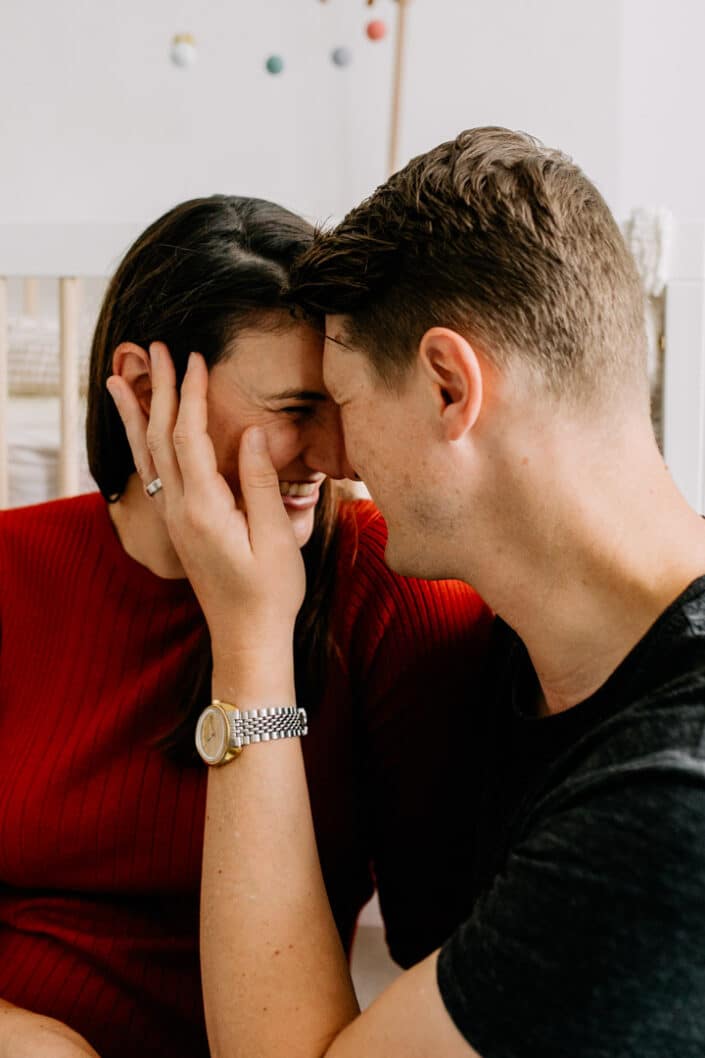 Expecting parents are cuddling close to each other and dad is holding his wife cheek. They are touching foreheads and mum is smiling. Maternity photo shoot in London. Ewa Jones Photography