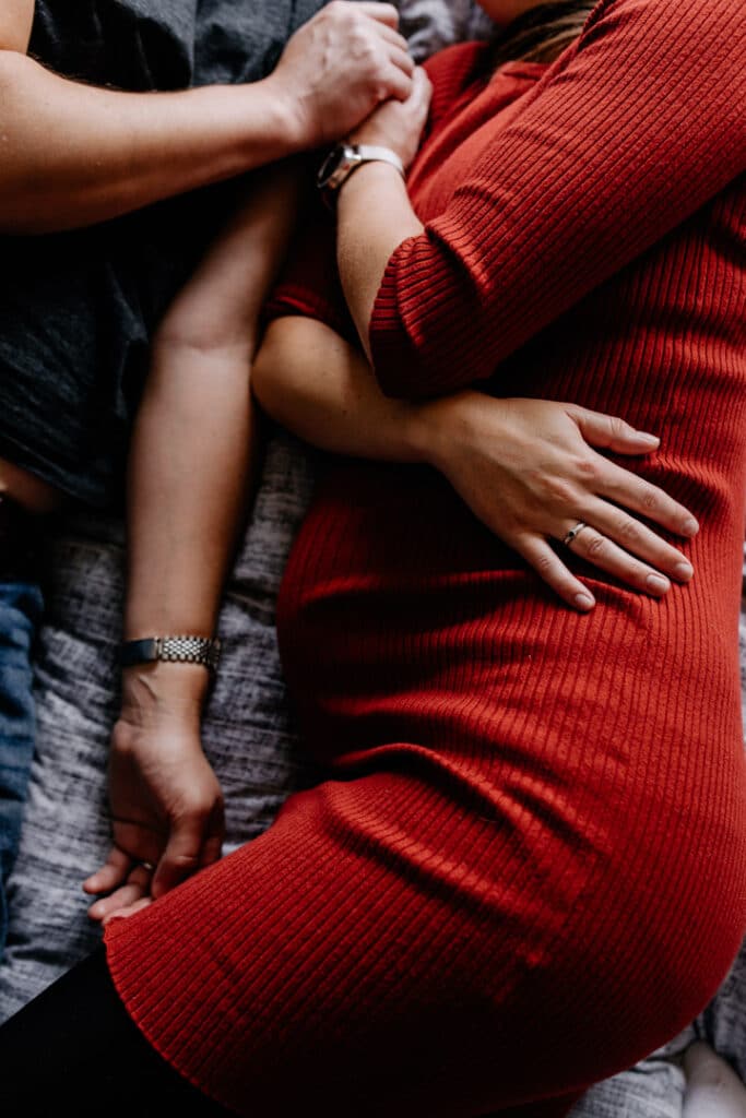 Expecting mum is laying on bed and holding baby bump. Lifestyle maternity photographer in London. Ewa Jones Photography