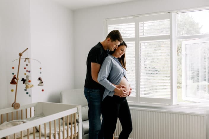 Mum and dad are standing in the baby nursery and they are holding baby bump. Maternity photographer in London. Ewa Jones Photography