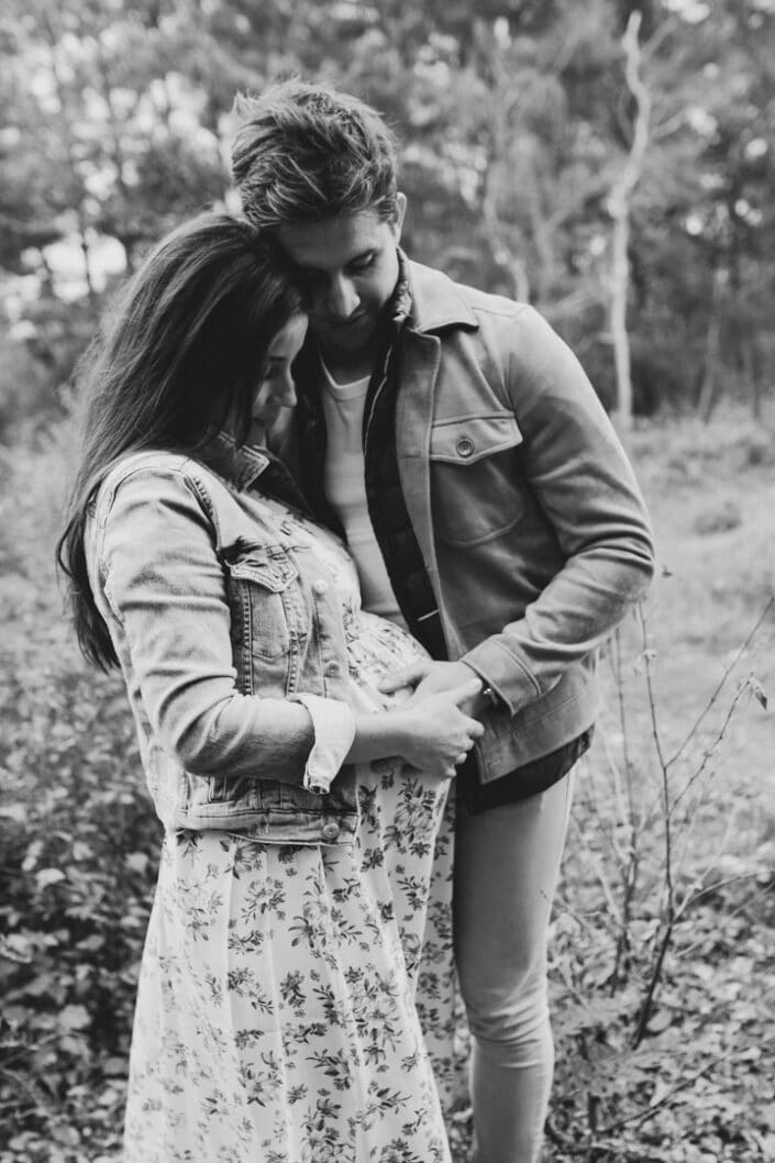 Black and white maternity photograph of parents cuddling to each other and holding baby bump. Maternity photographer in Hampshire. Ewa Jones Photography