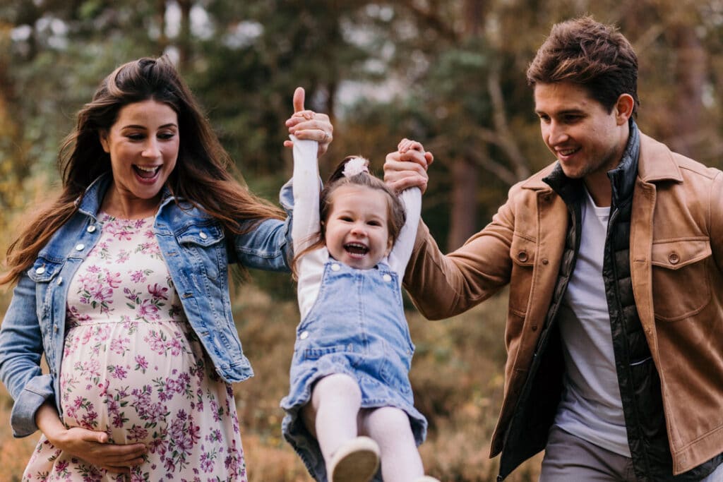 Expecting parents are lifting their older daughter in the air. My favourite maternity photographs of 2021 Maternity photographer in Hampshire. Ewa Jones Photography