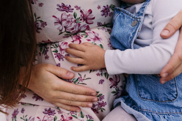 pregnant mum is holding her bump and her older daughter is touch bump too. My favourite maternity photographs of 2021. Maternity photography in Hampshire. Ewa Jones Photography