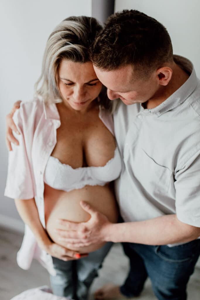 Mum and dad are holding baby bump. Mum is wearing a pink shirt and dad is wearing grey shirt. Maternity photo shoot in Hampshire. Ewa Jones Photography