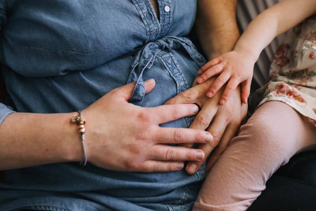 Mum, dad and older daughter are both holding baby bump. Maternity photography in Basingstoke, Hampshire. Ewa Jones Photography