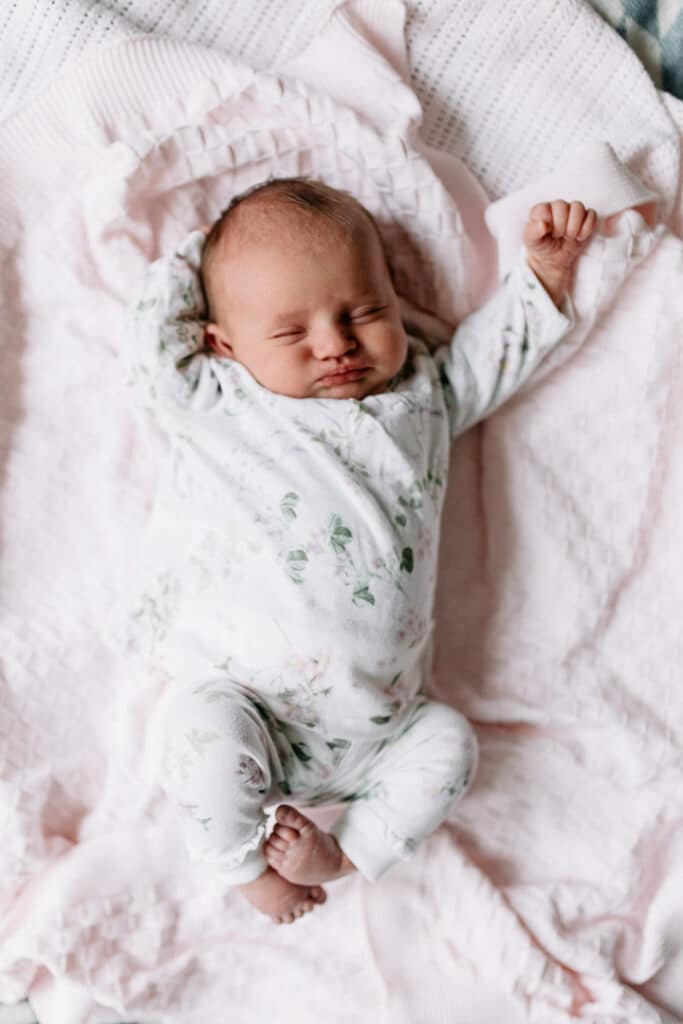 Newborn baby girl is laying on the blankets and she is stretching. Lifestyle newborn photo session in Hampshire. Ewa Jones Photography