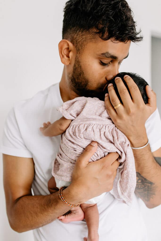 Dad is holding his newborn baby girl and kissing her on her head. Lifestyle photosession. Newborn photographer in London. Ewa Jones Photography