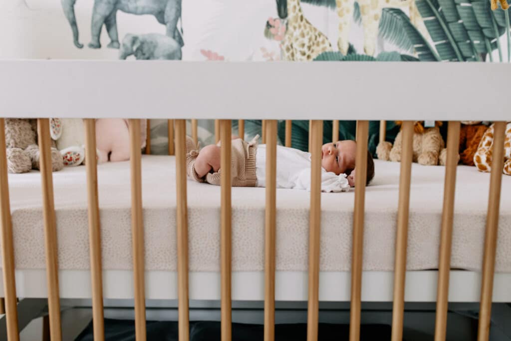 Newborn baby girl is laying in her baby cot and looking up. She has a lovely safari theme nursery. Lifestyle newborn photo shoot in Basingstoke, Hampshire. Ewa Jones Photography