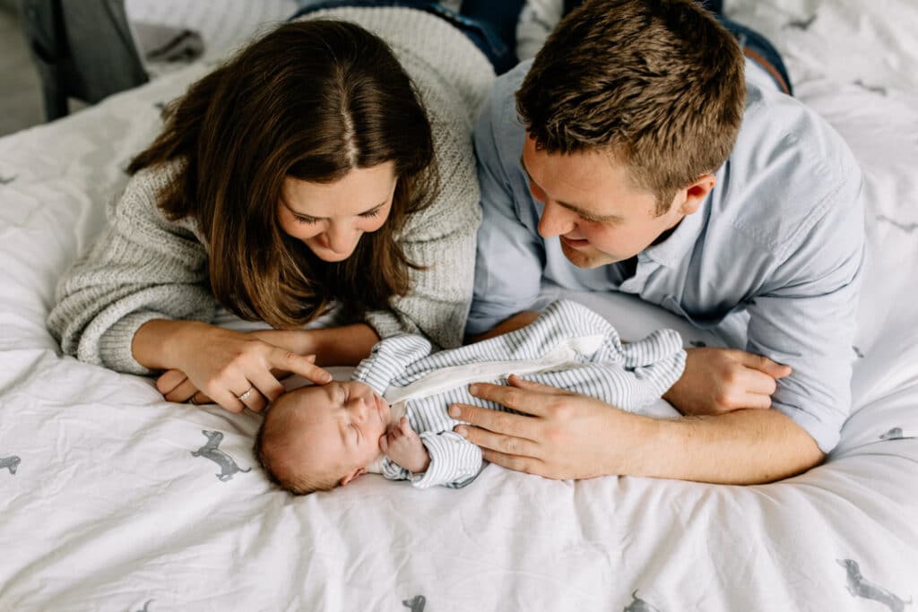 mum and dad are laying on bed and looking down at their newborn baby boy. Newborn photographer in Basingstoke. Ewa Jones Photography