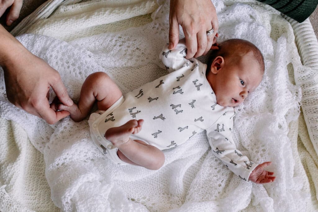 Newborn baby boy is laying on blankets and mum and dad are holding his hand and foot. Lifestyle natural photo shoot. Ewa Jones Photography