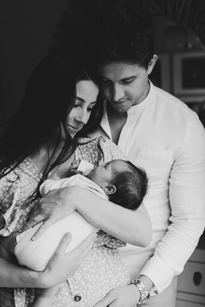 mum and dad are cuddling up to their newborn baby girl. Black and white image. Lifestyle newborn photo shoot in Basingstoke, Hampshire. My favourite newborn photographs of 2021. Ewa jones Photography