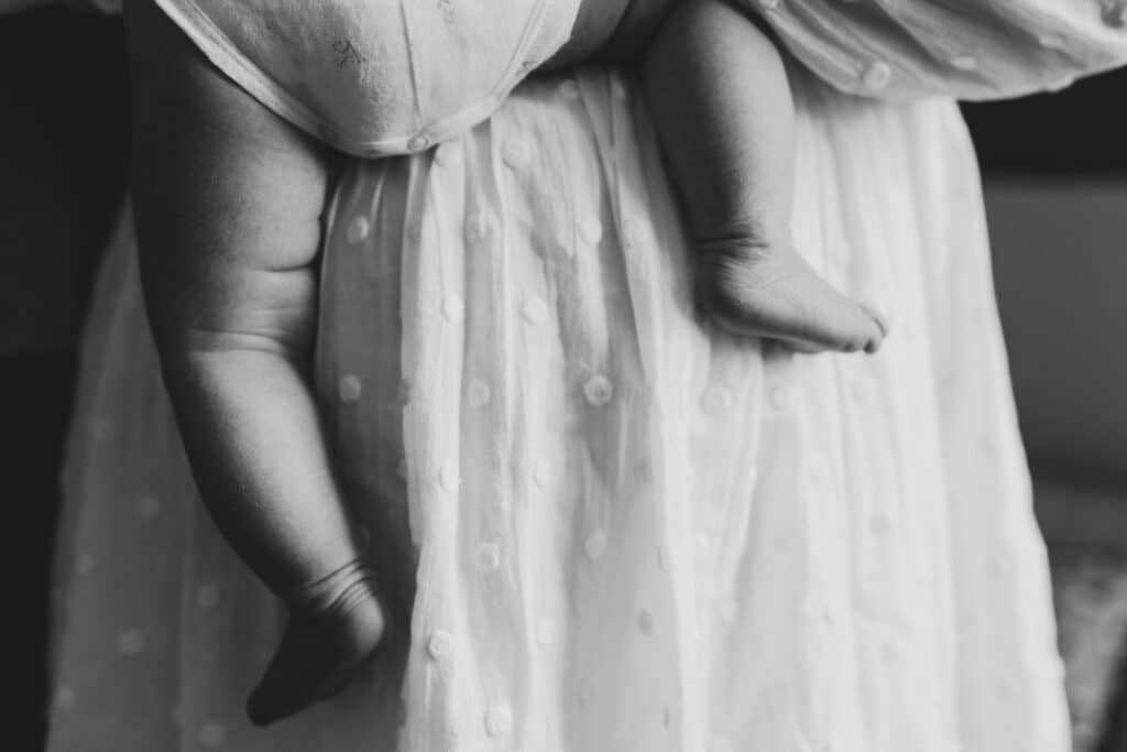Black and white image of newborn baby feet. Mum is holding the newborn baby and the feet are just hanging down. Black and white candid image. Newborn photographer in Hampshire. Ewa Jones Photography