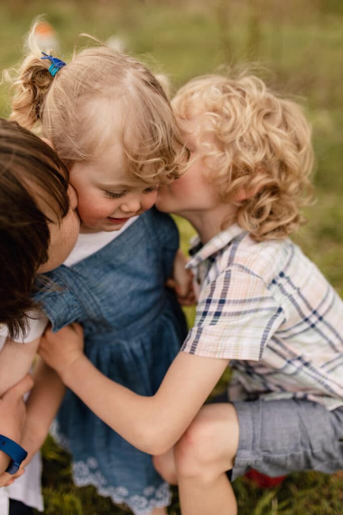 Two brothers are kissing their younger daughter. Girl is wearing lovely blue denim jacket and boys are wearing t-shirts. Family photo shoot in Basingstoke, Hampshire, Basingstoke photographer. Ewa Jones Photography