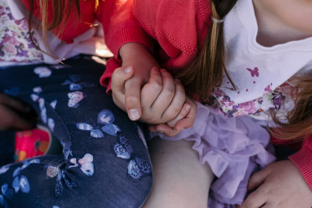 Two sisters are holding hands. It is a lovely summer day and girls are wearing lovely summer outfits. Family photo shoot in Hampshire. Family photography in Basingstoke, Hampshire. Ewa Jones Photography