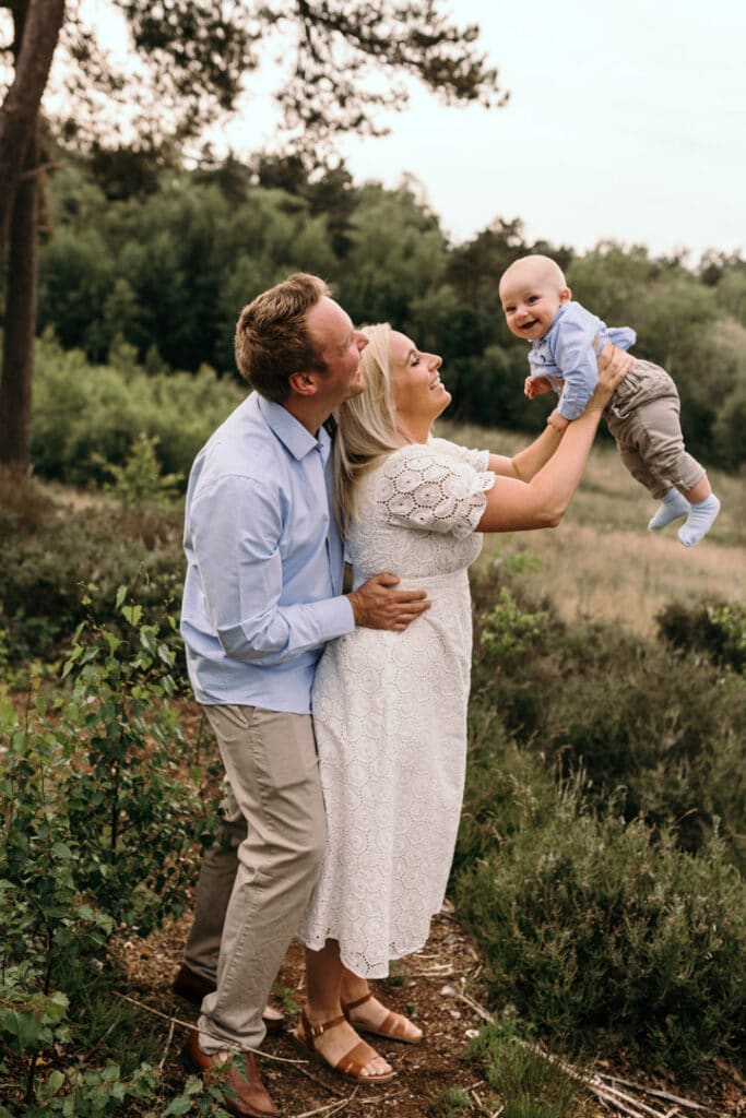 mum is holding her little boy in the air and the boy is laughing. dad is behind mum smiling and looking at his son. Summer family photo shoot in Hampshire. Hook family photographer. Ewa Jones Photography