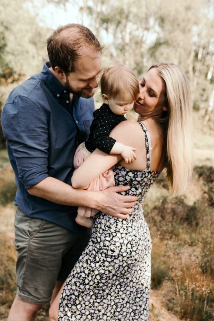 Family of three is holding close to each other and mum and dad are looking at the little baby girl. Summer family photo shoot in Hampshire. Basingstoke photographer. Ewa Jones Photography