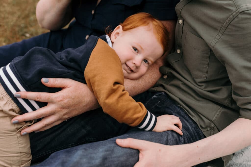 Little boy is cuddling to his mum. He is wearing blue and orange jacket. Late summer family photo session in Hampshire. Ewa Jones Photography