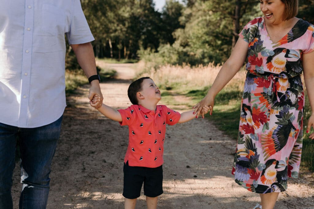 Mum, dad and son are holding hands together. Mum and son are looking at each other and laughing. Lovely natural lifestyle photo session. Hampshire photographer. Ewa Jones Photography