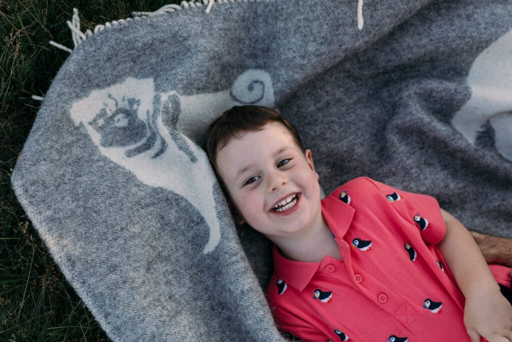 Little boy is laying on the blanket and looking up. Mum is tickling him and he is laughing as well. Family photo shoot in Hampshire. Ewa Jones Photography