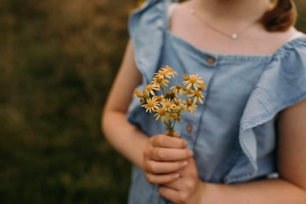 Girl is holding a yellow flowers. She is wearing jean outfit. It's a summer day in Basingstoke. Basingstoke photographer. Ewa Jones Photography